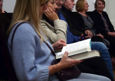 Kobieta w niebieskim swetrze siedząca z otwartą książką w rękach.